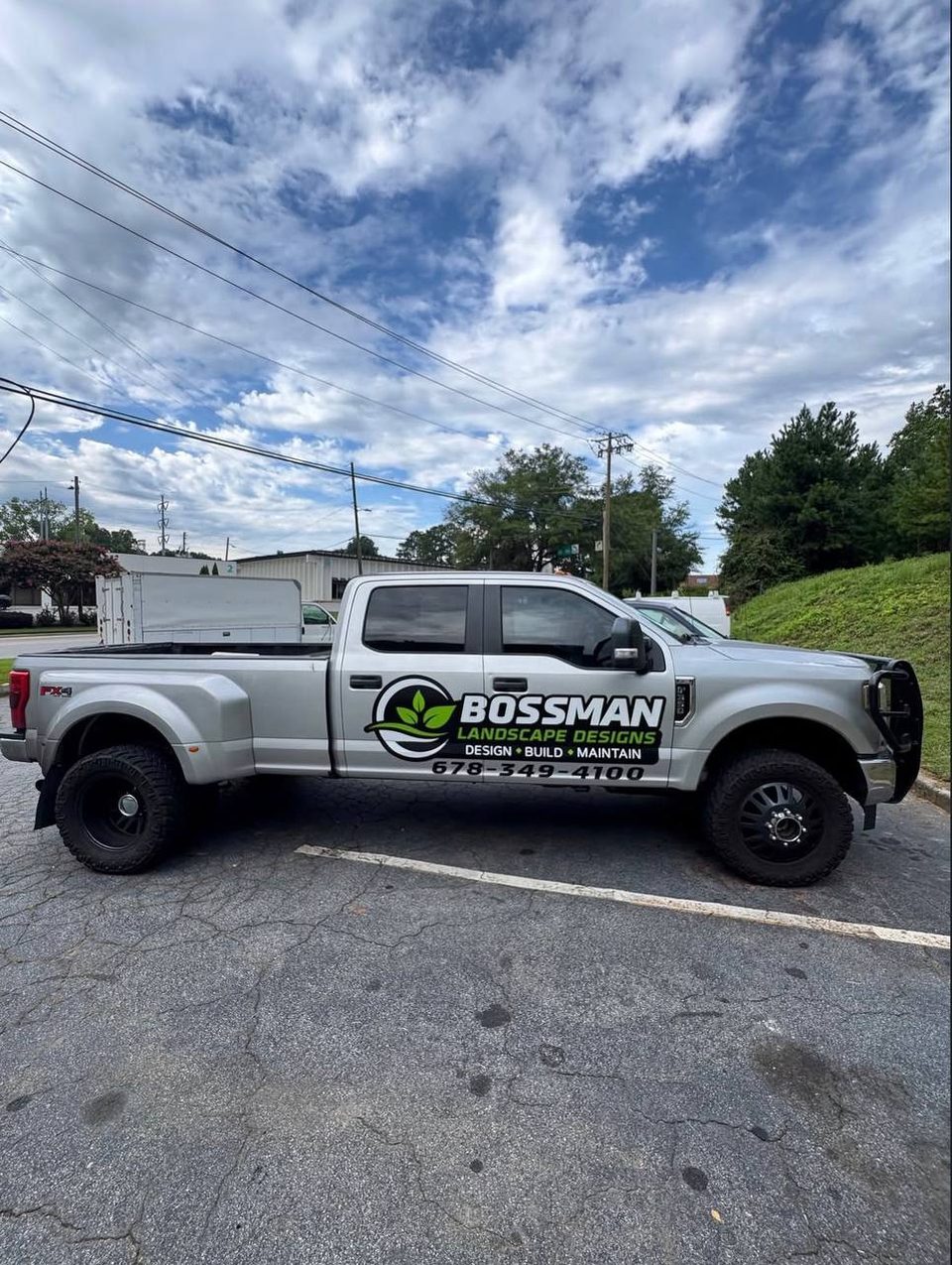 Silver dually pickup with a landscape design company logo and phone number on the door