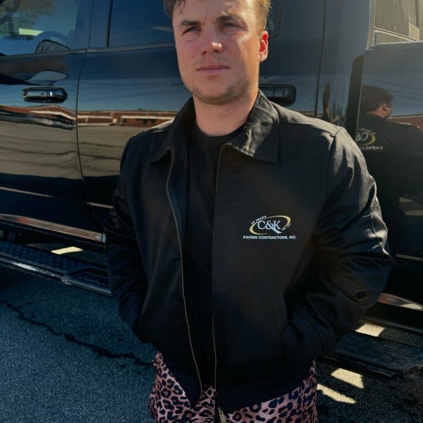 Crew member in a black work jacket with an embroidered paving company logo