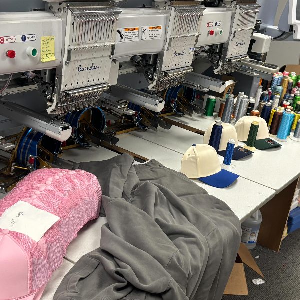 Hats, thread and a hoodie lined up at the embroidery machines